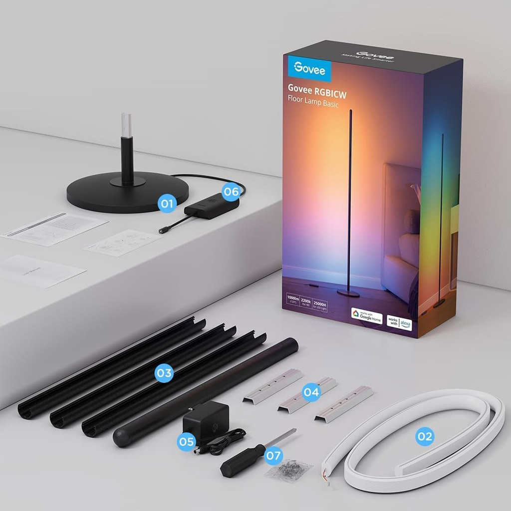 Unboxed components of the Govee RGBICW Floor Lamp Basic are neatly arranged beside its packaging, which shows the lamp casting multicoloured light in a room. Visible parts include the lamp base, LED light strip, black structural segments, reflective channels, power adapter, control unit, and a screwdriver with screws. Instruction manuals are placed nearby. The packaging highlights features like 1500lm brightness, a 2700K–6500K colour temperature range, and compatibility with Google Home and Alexa.