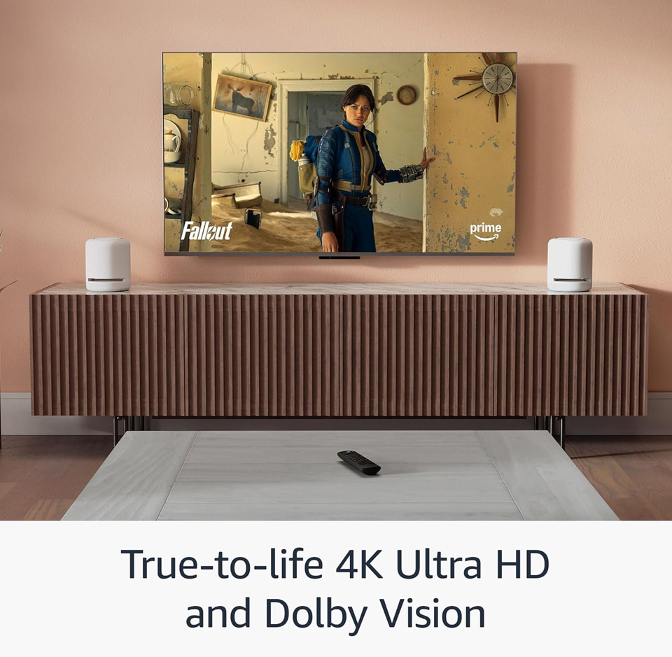 Wall-mounted TV in a modern living room displaying a scene from Fallout on Prime Video, demonstrating true-to-life 4K Ultra HD picture quality with Dolby Vision, with a media console and remote visible below.