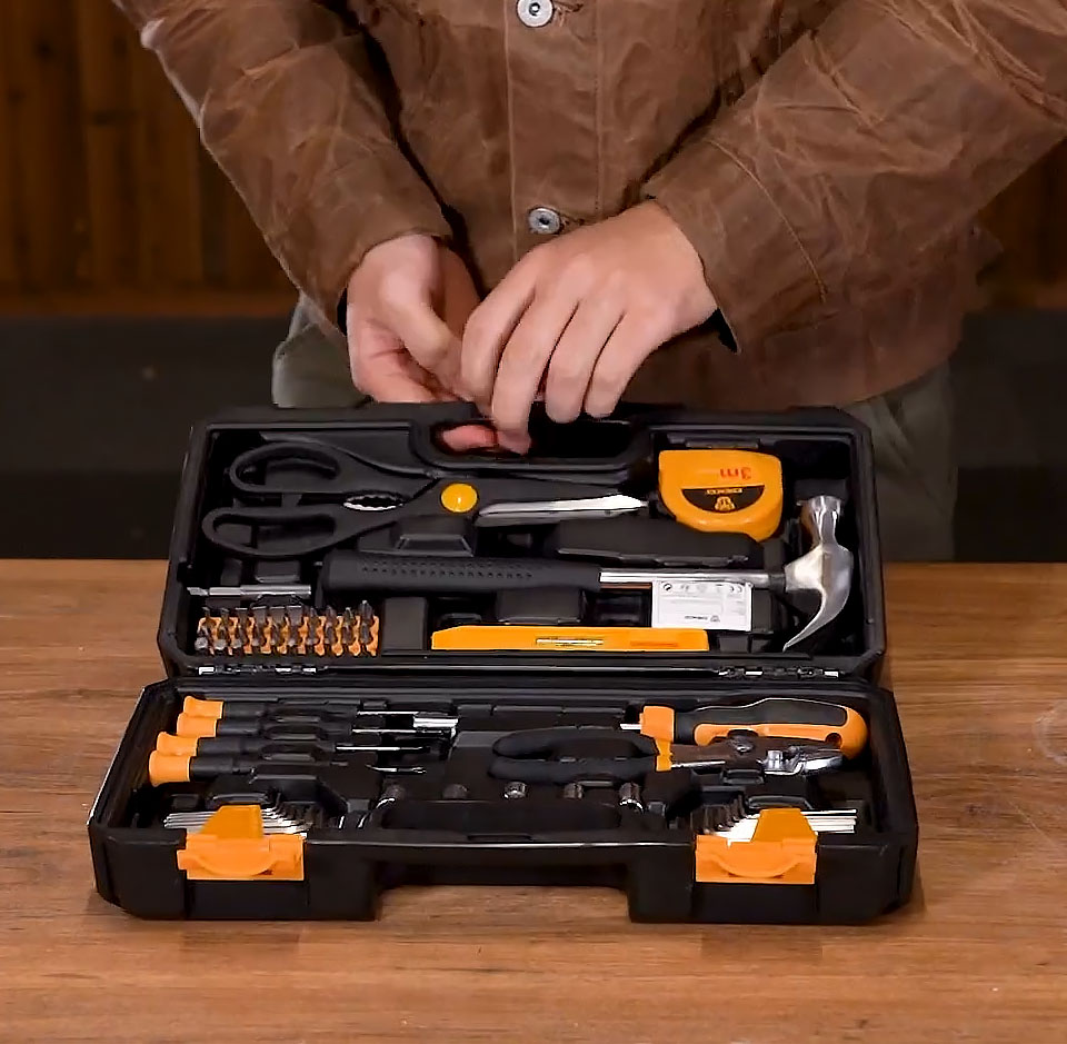 A black and yellow 62-piece DIY home repair tool kit open on a wooden surface, showing assorted hand tools including a hammer, tape measure, pliers, screwdrivers, bits and other tools neatly organised inside a moulded plastic carry case.