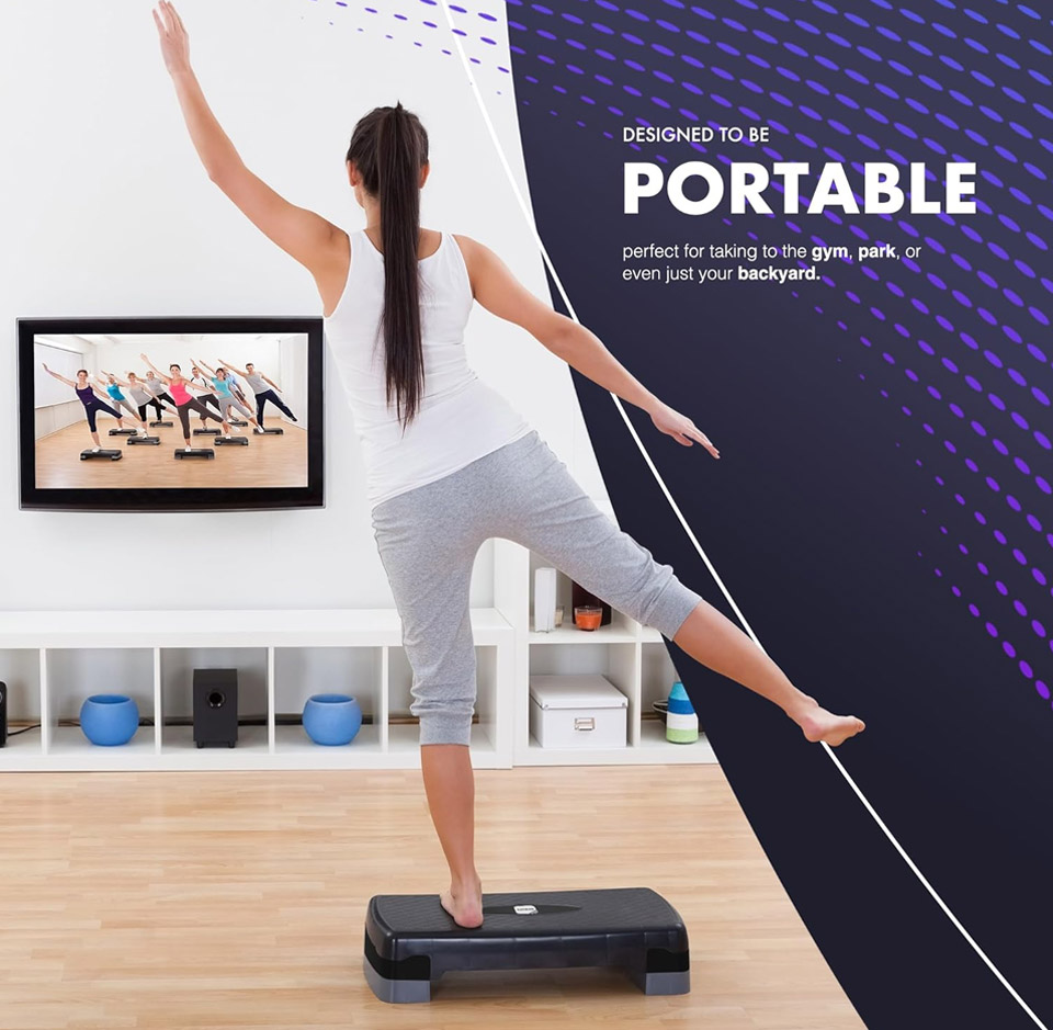 A black and dark grey adjustable aerobic step platform for home workouts on a light wood floor. A person wearing grey leggings and a white tank top is balancing on one foot on the step, lifting their other leg and arms for a fitness pose. A TV screen on a white shelf shows a group doing step exercises, and purple graphic text on the right reads “designed to be portable,” illustrating the exercise step’s use for cardio and aerobics.