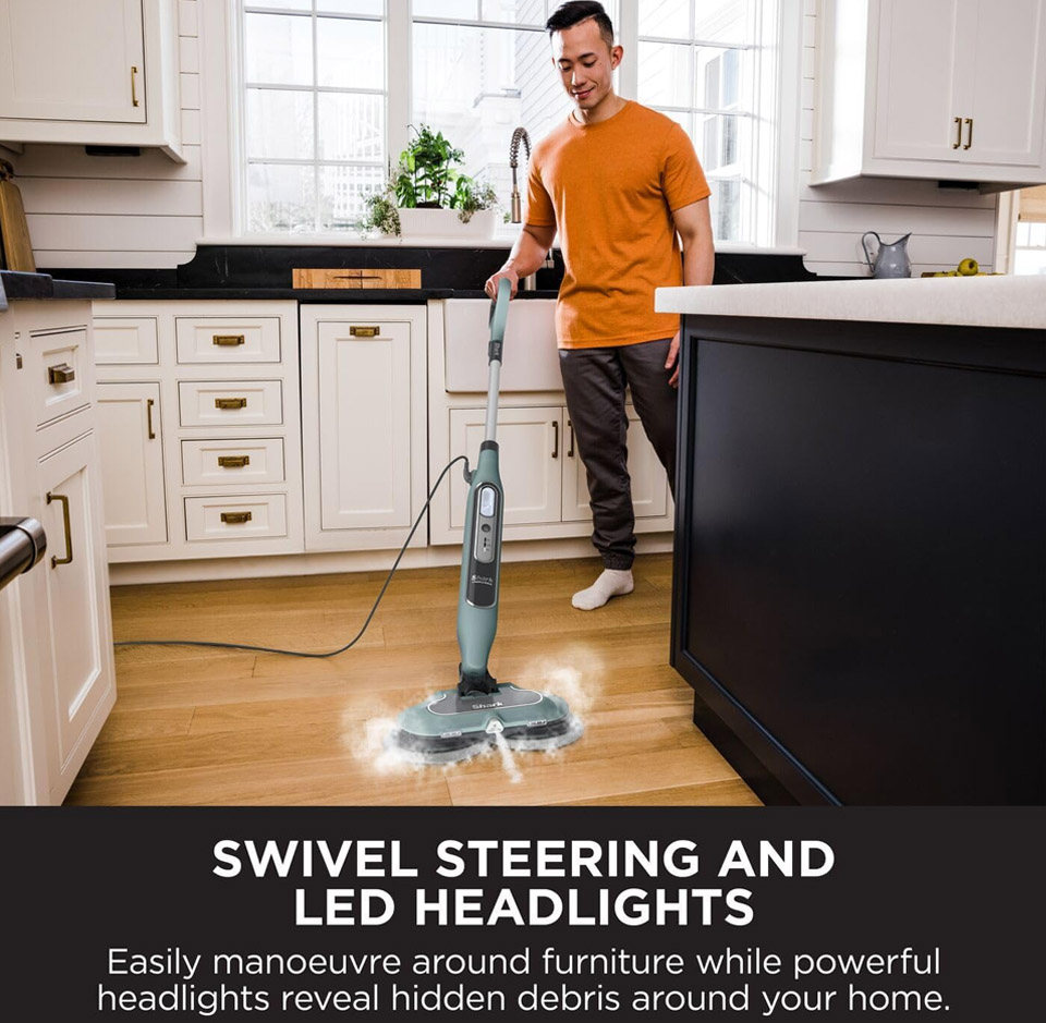 Person using a Shark Automatic Steam and Scrub Mop on a wooden kitchen floor, with the steam mop’s dual rotating pads visible cleaning the surface.
