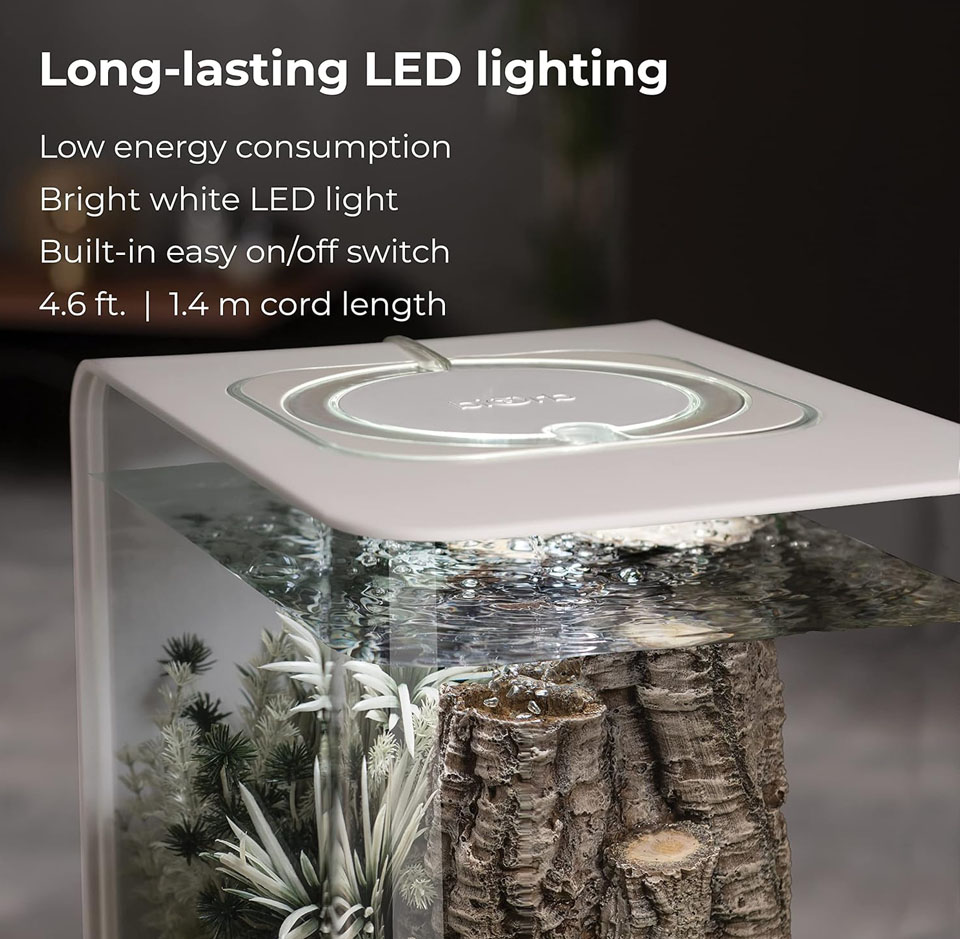 Modern aquarium with a sleek white top featuring a built-in circular LED light. Inside the tank, artificial plants and textured logs create a decorative underwater scene. The water is filled to the top, and the bright white LED lighting casts a clean, vibrant glow. Overlay text highlights features: “Long-lasting LED lighting,” “Low energy consumption,” “Bright white LED light,” “Built-in easy on/off switch,” and “4.6 ft.  1.4 m cord length.