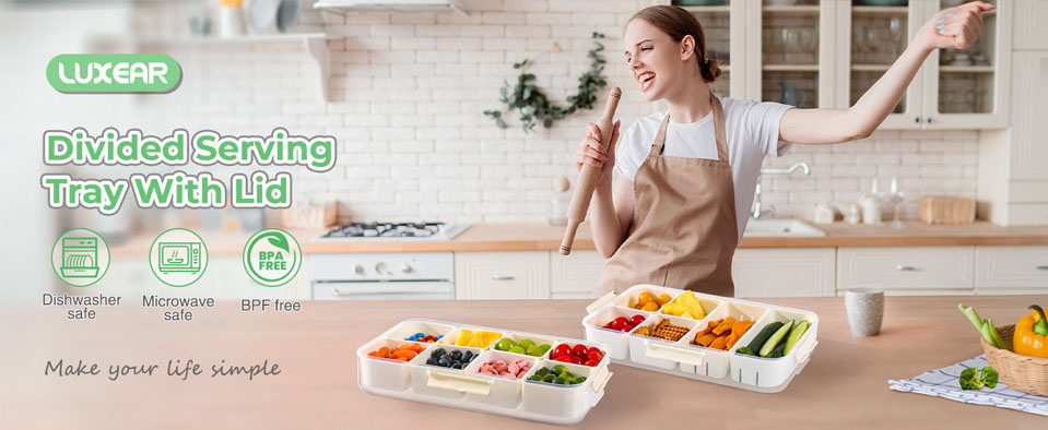 A woman in a kitchen wearing a brown apron smiles while holding a rolling pin behind two white divided serving trays filled with colourful fruits, vegetables, and snacks. Each tray has multiple compartments with clear lids. Text on the image highlights features including dishwasher‑safe, microwave‑safe, BPA‑free, and BPF‑free, alongside the product name “Luxear Divided Serving Tray With Lid.”